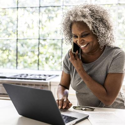 A smiling women on her phone and looking at a laptop